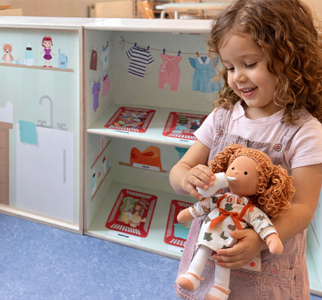 Pige leger med dukke foran reol med møbelfolie